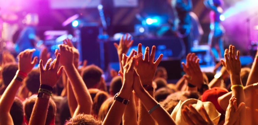 Personnes dans une foule d'un spectacle de musique, qui lèvent les mains devant une scène.